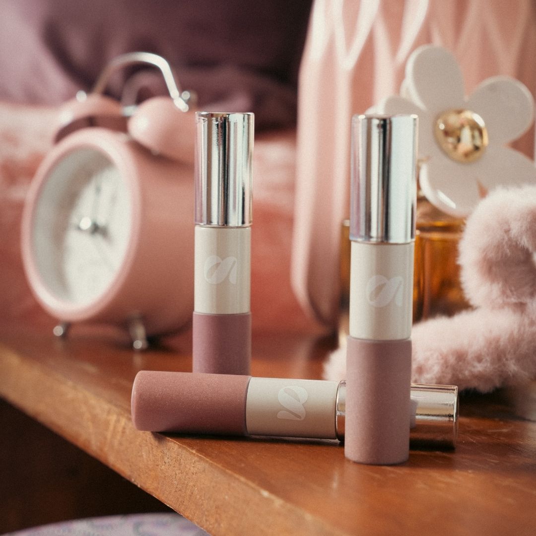 Three lipsticks on a wooden surface with a blurred background. Shade Florencia