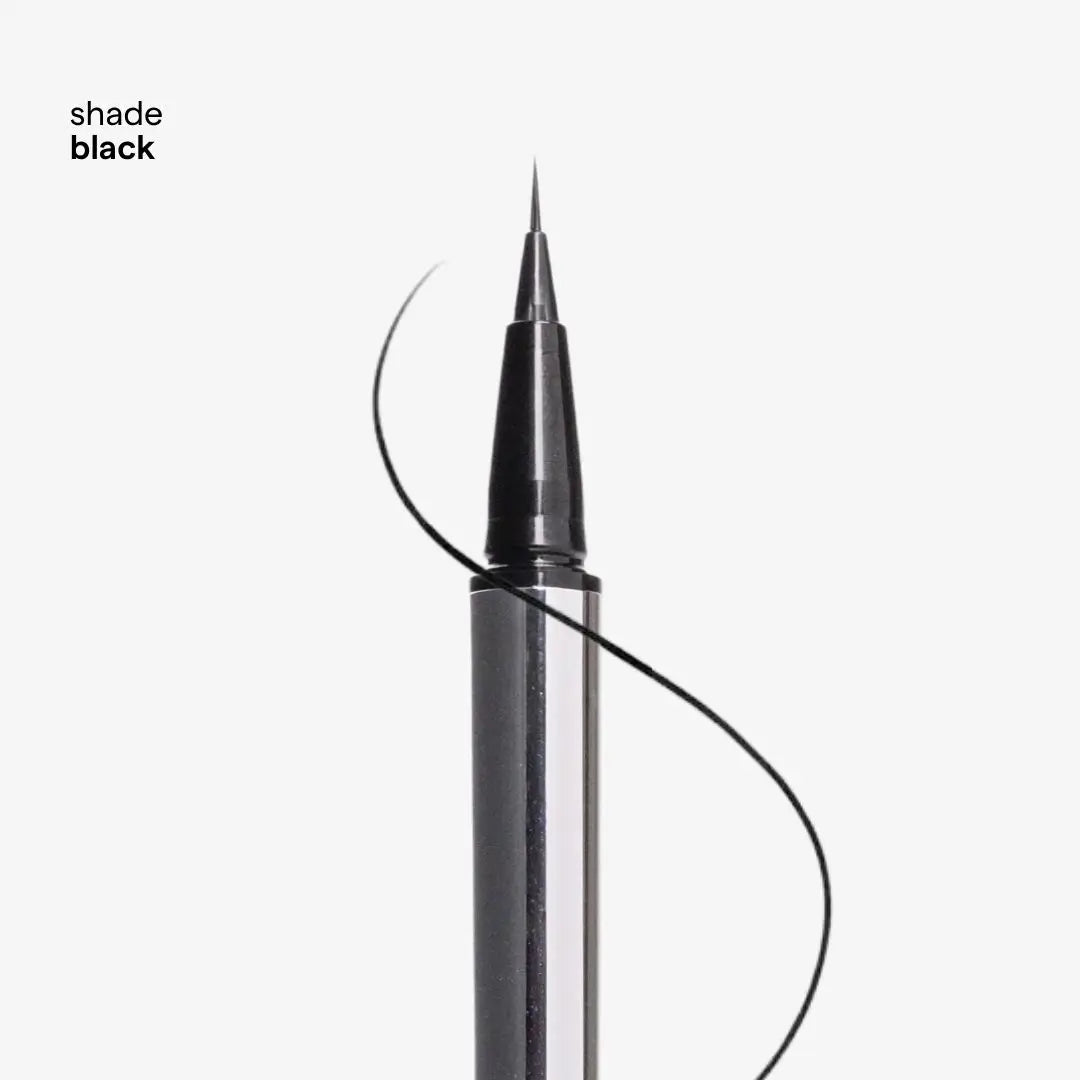 A close-up of a black liquid eyeliner pen with a fine tip, shown against a light gray background with the text 'shade black' in the upper left. A thin black line is drawn to demonstrate the color and application.