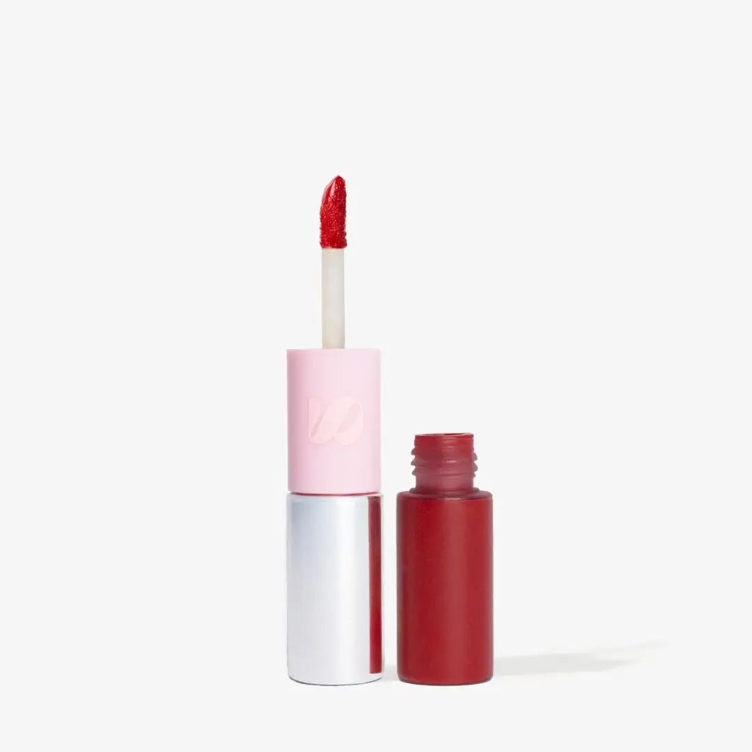 A liquid lipstick in a pale pink and silver tube with the applicator open, shown next to the open dark red bottle on a clean white background. Shade Rubi