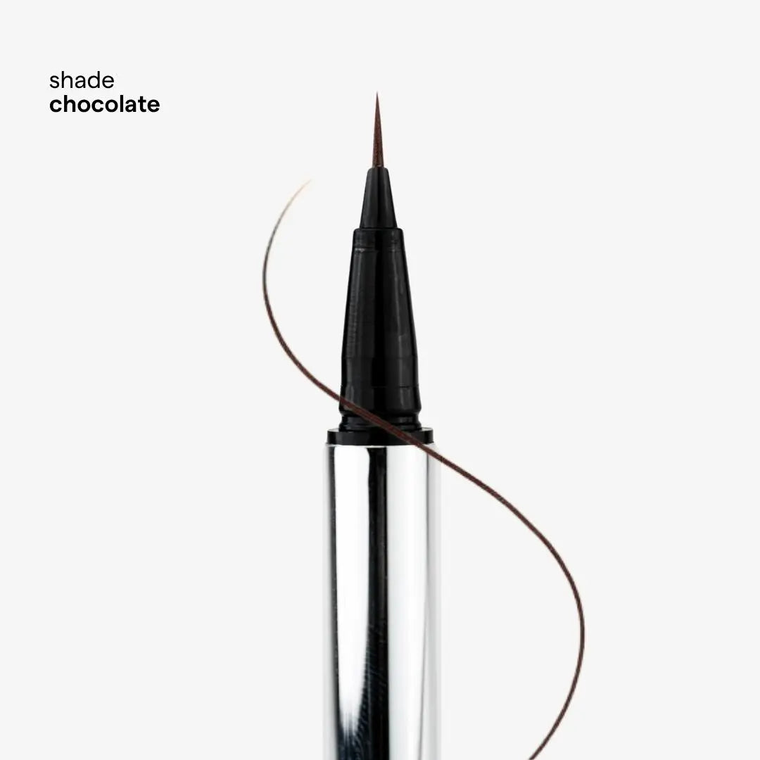 A close-up of a fine-tip liquid eyeliner pen with a silver barrel, shown against a light gray background with the text 'shade chocolate' in the upper left. A thin brown line curves behind the pen to indicate the color.