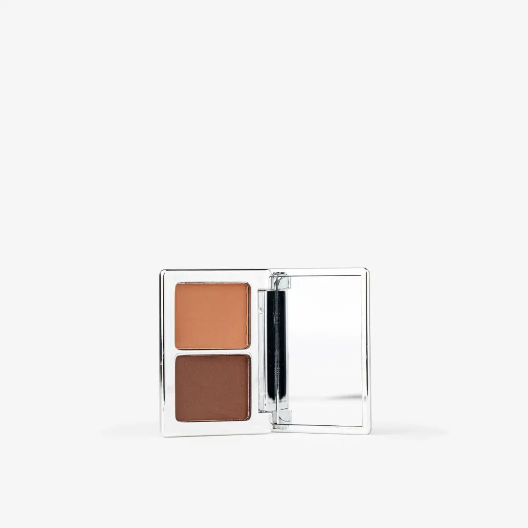 A square makeup compact with two pressed powder pans, one in a warm tan shade and the other in a medium brown shade, shown open against a plain white background. Creamy Chocolate