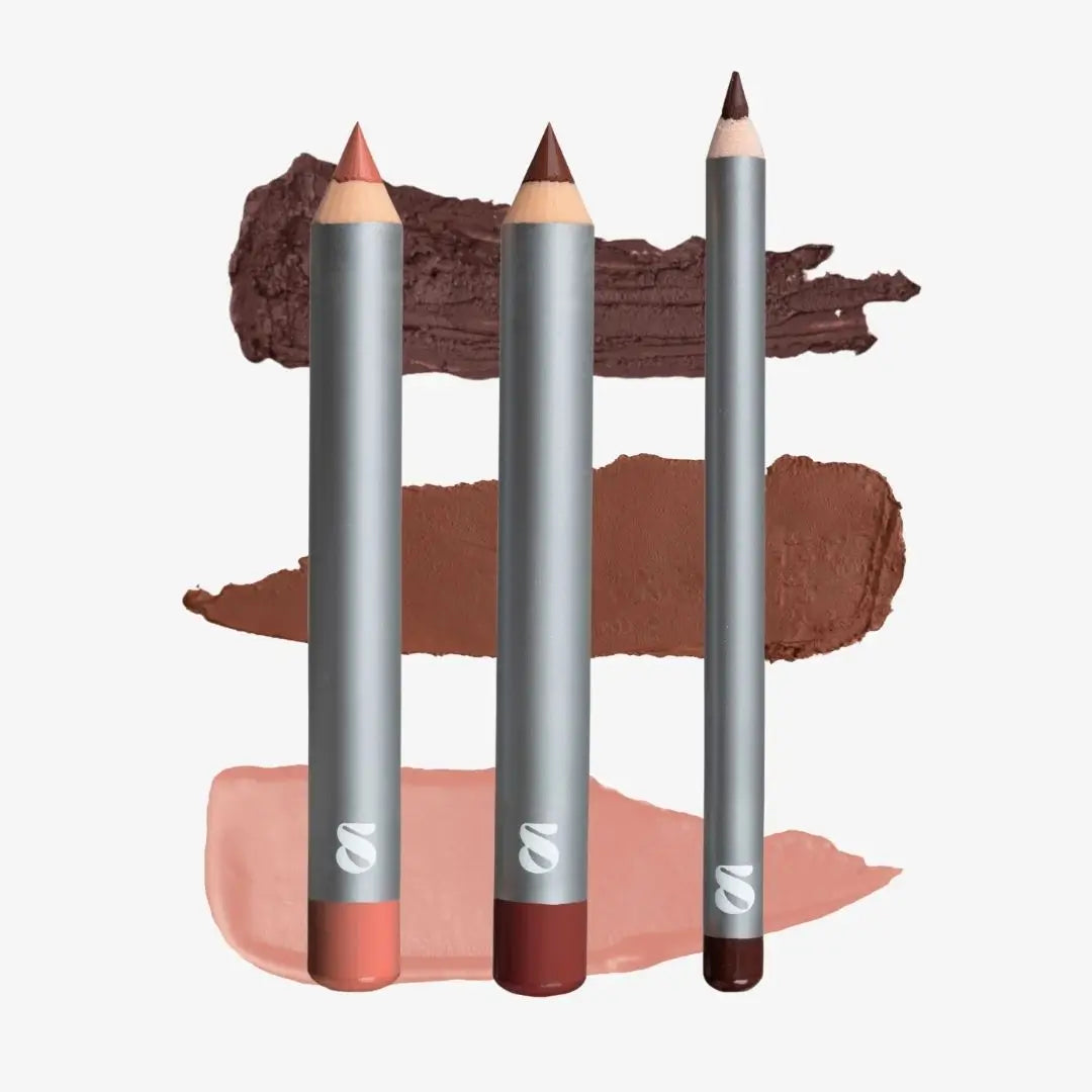 Three lip color pencils with silver bodies are displayed vertically in front of three corresponding makeup swatches in dark brown, medium brown, and soft pink on a light gray background. Shade chocolate