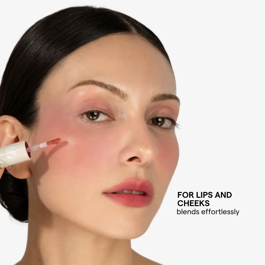 Close-up of a woman with dark hair applying a pink lip and cheek cosmetic from a white tube, with text reading 'FOR LIPS AND CHEEKS blends effortlessly' on a light gray background. Shade Florencia