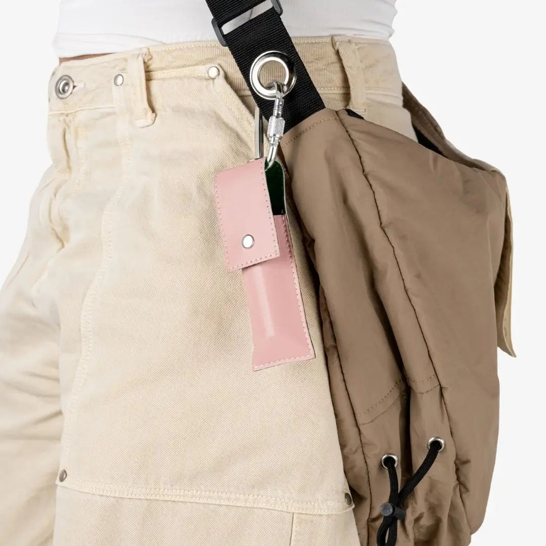 A close-up of a beige crossbody bag with a black strap, silver hardware, and a pink leather card holder, worn over cream cargo pants. Shade Florencia