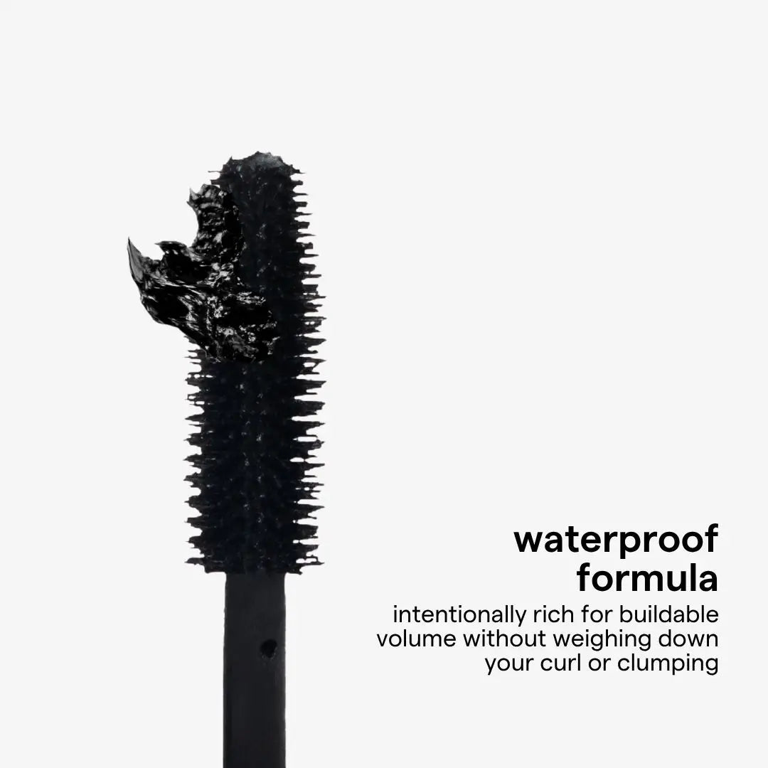 A close-up of a black mascara wand showing thickened, textured formula on the brush, with Spanish text on a light gray background reading 'fórmula waterproof' and descriptive copy.