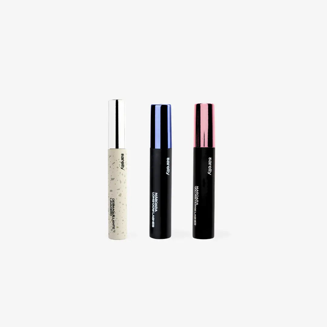 Three slim cosmetic tubes standing upright on a light gray background: a white tube with black speckles and a silver cap, a black tube with a blue cap, and a black tube with a pink cap. The brand name 'sarelly' is visible on each tube.