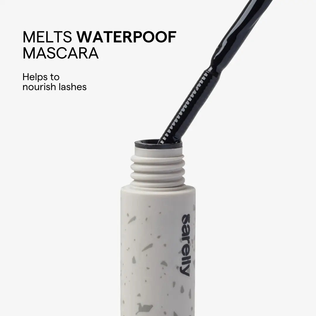 A close-up of a mascara tube with the wand inserted, shown on a light gray background with text reading 'MELTS WATERPROOF MASCARA' and 'Helps to nourish lashes.' The tube is white with subtle gray speckling, and the wand is black.